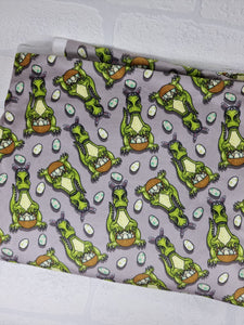 Green dinosaurs wearing bunny ears and carrying easter baskets on a grey background. Squish fabric sold by the half metre